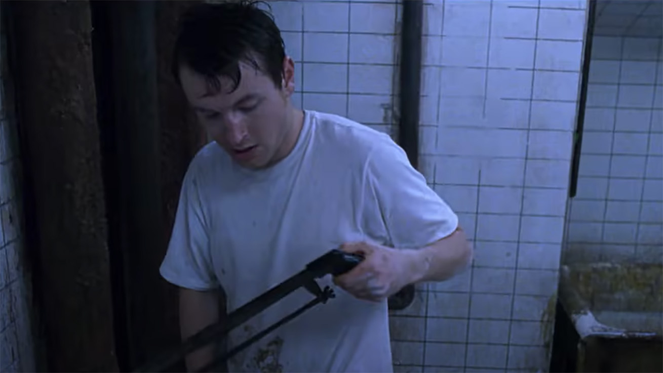 Leigh Whannell holding a hacksaw from Saw (2004)
