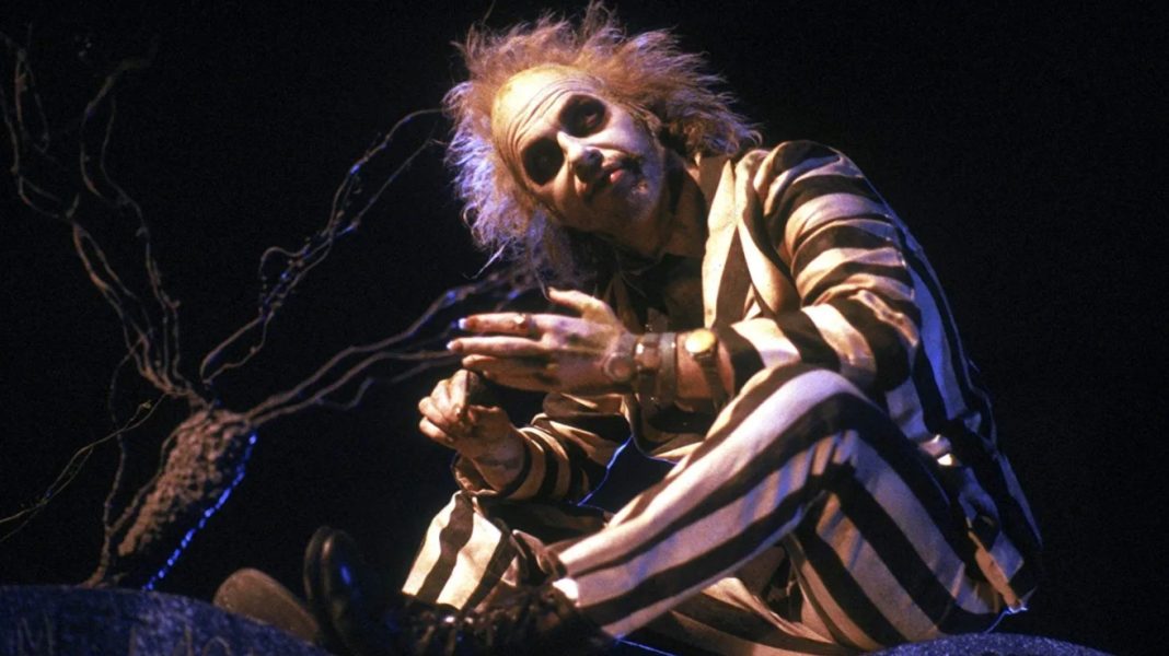 Michael Keaton as Beetlejuice sitting on a gravestone