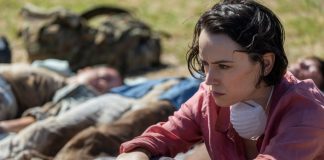 A woman sits next to dead bodies while wearing a mask around her neck in We Bury the Dead