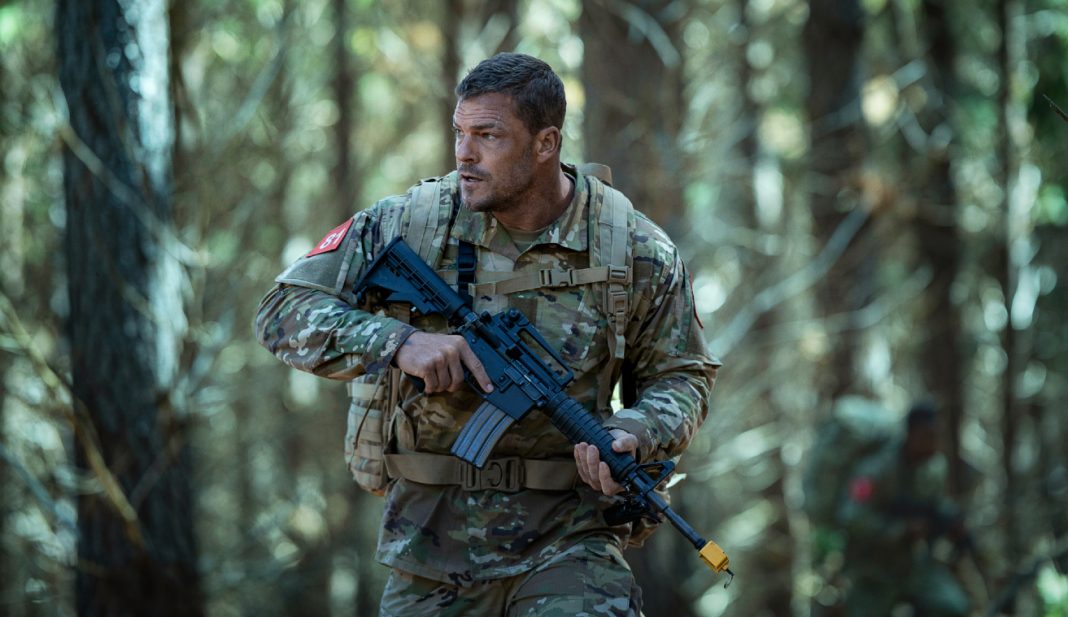 81 (Alan Ritchson) holds a rifle while walking through a forest in Netflix's War Machine