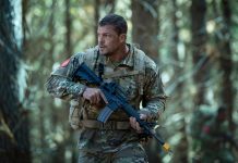 81 (Alan Ritchson) holds a rifle while walking through a forest in Netflix's War Machine