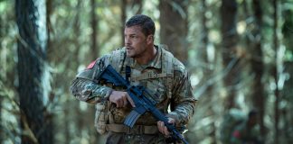 81 (Alan Ritchson) holds a rifle while walking through a forest in Netflix's War Machine