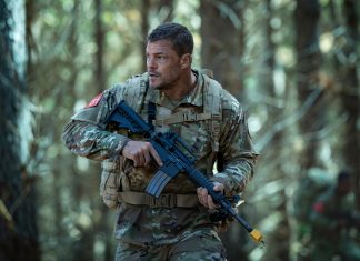 81 (Alan Ritchson) holds a rifle while walking through a forest in Netflix's War Machine