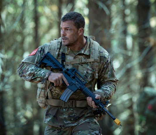 81 (Alan Ritchson) holds a rifle while walking through a forest in Netflix's War Machine