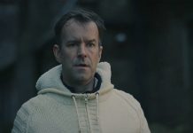 A man wearing a white sweater stares at someone in a graveyard in Watch Me Sleep