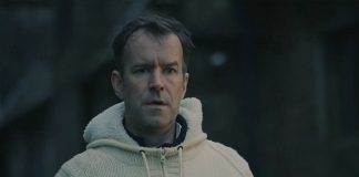 A man wearing a white sweater stares at someone in a graveyard in Watch Me Sleep