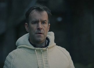 A man wearing a white sweater stares at someone in a graveyard in Watch Me Sleep