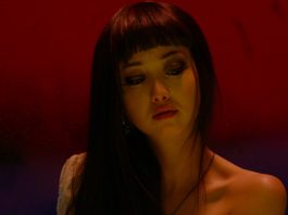 Against a red and purple background, a woman looks down in Helter Skelter (2012)