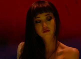 Against a red and purple background, a woman looks down in Helter Skelter (2012)