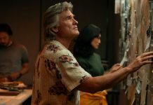 Wearing a floral shirt, Lee Shaw (Kurt Russell) looks at a wall covered in documents in Monarch Legacy of Monsters Season 2, Episode 4 'Trespass'