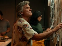 Wearing a floral shirt, Lee Shaw (Kurt Russell) looks at a wall covered in documents in Monarch Legacy of Monsters Season 2, Episode 4 'Trespass'