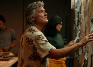 Wearing a floral shirt, Lee Shaw (Kurt Russell) looks at a wall covered in documents in Monarch Legacy of Monsters Season 2, Episode 4 'Trespass'