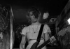 A woman plays the guitar while on stage in The Yellow Bellies