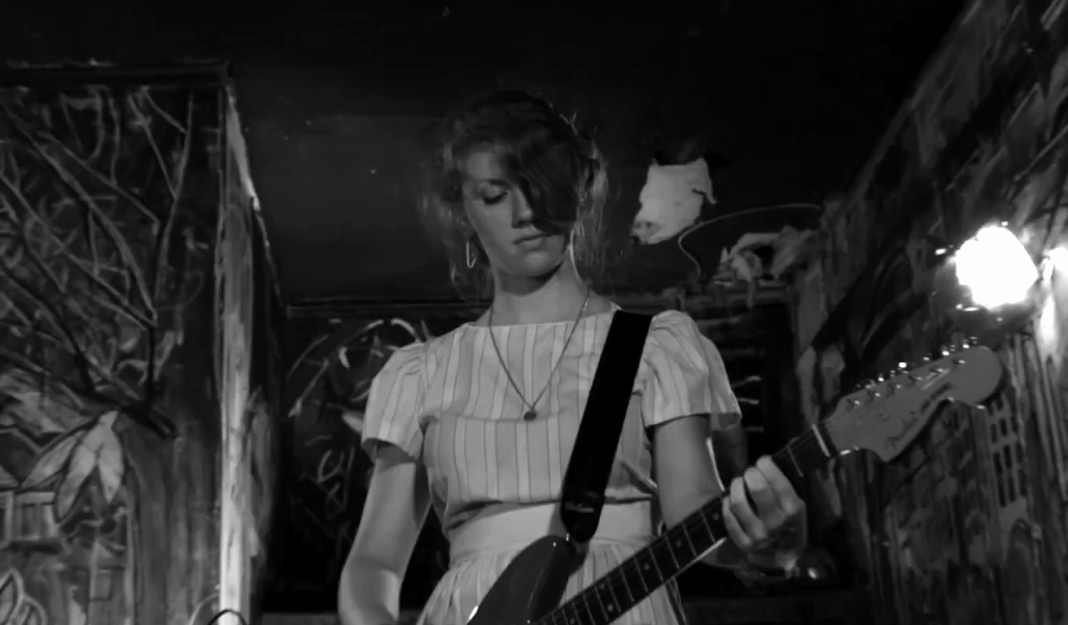A woman plays the guitar while on stage in The Yellow Bellies A woman plays the guitar while on stage in The Yellow Bellies