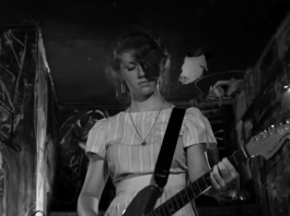 A woman plays the guitar while on stage in The Yellow Bellies