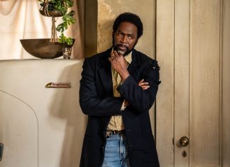 Boyd stands in the kitchen next to the fridge, thinking, in FROM Season 4 Episode 6