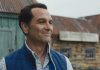 Tom Loftis smiles as he looks around outside in Widows Bay Season 1