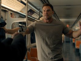 Reacher holds his hands up at gunpoint on a subway in Reacher Season 4
