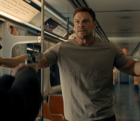 Reacher holds his hands up at gunpoint on a subway in Reacher Season 4