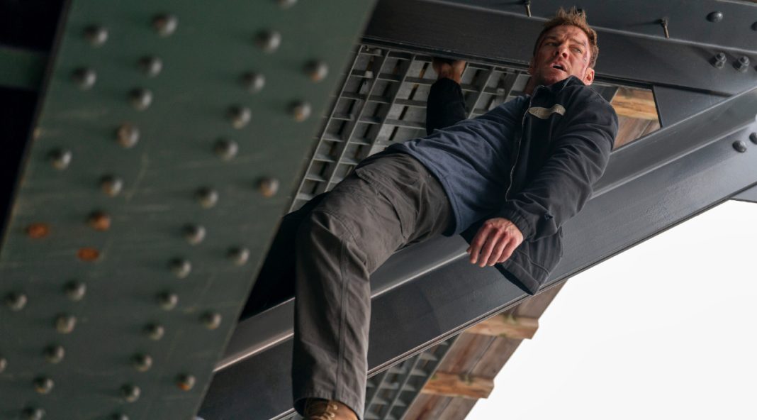 Reacher holds onto a beam under a bridge in Reacher Season 4