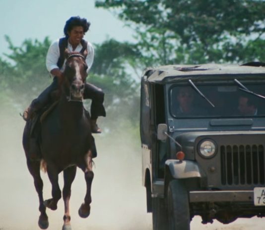 A man on horseback rides next to a Jeep in Roaring Fire 1981