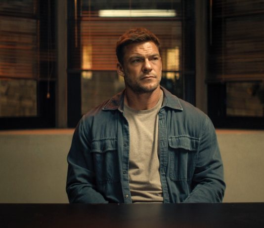 Reacher sits at a police desk in Reacher Season 4